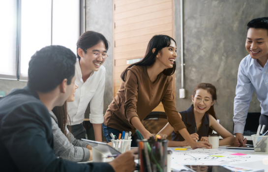 TP team in a collaborative meeting, smiling and discussing ideas around a table.