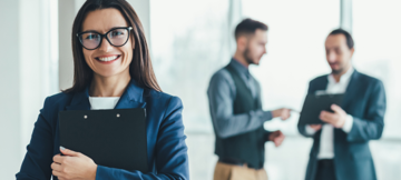 Smiling businesswoman holding clipboard with colleagues talking in background